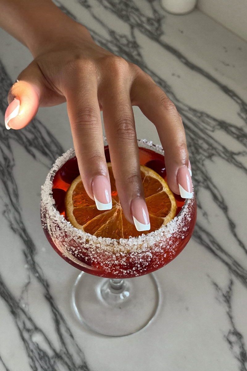 Hand placing an orange wheel garnish on a cranberry orange margarita